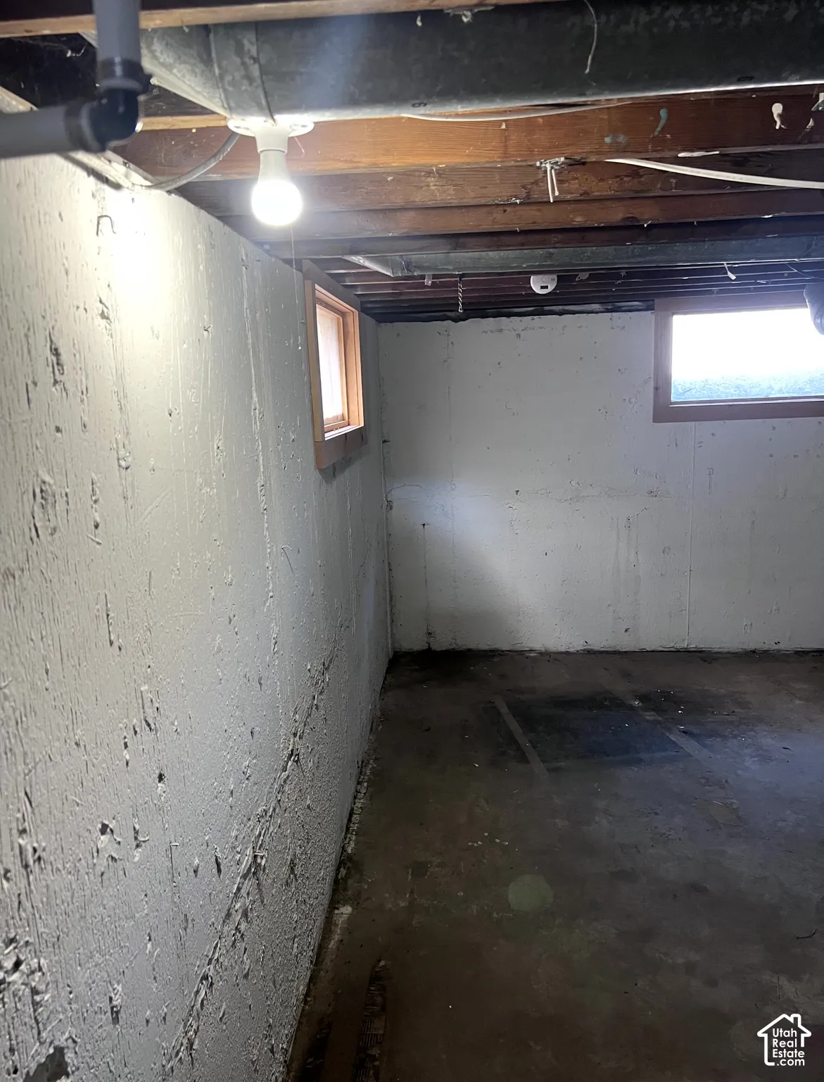 Unfinished basement space featuring exposed ceiling joists, concrete walls, two windows with wood trim, and a concrete floor