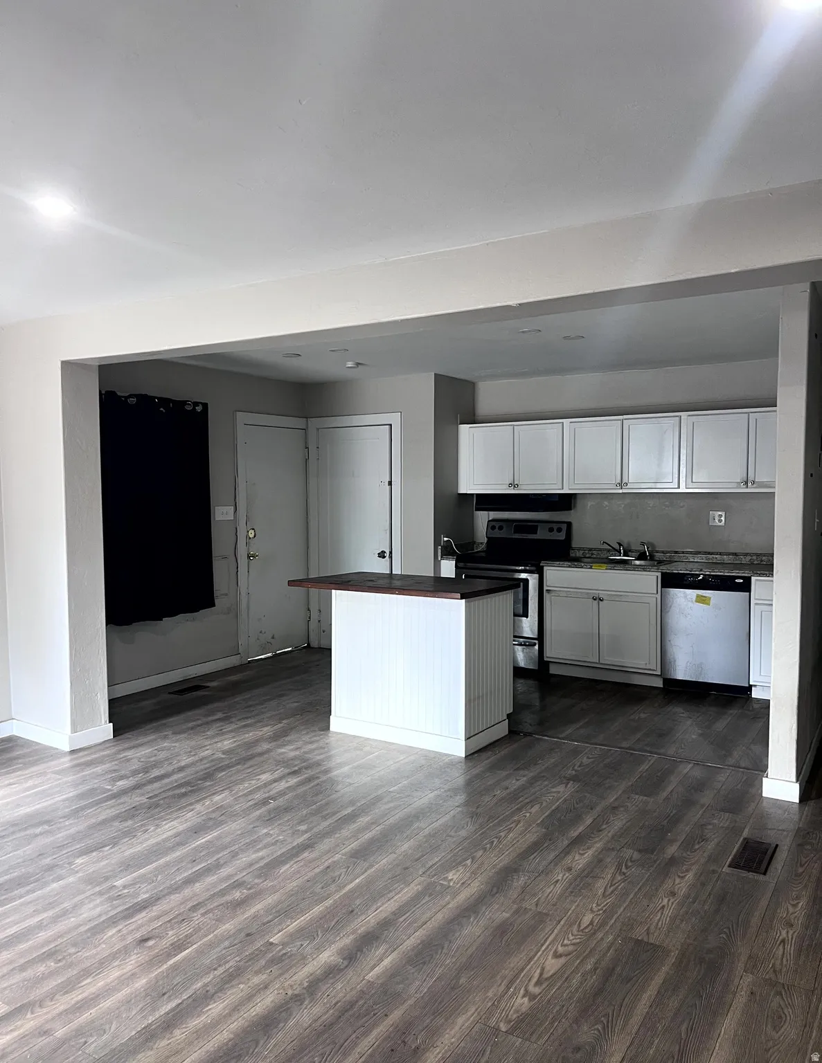 Open-concept living area featuring wood-finish flooring, recessed lighting, and a white kitchen island with a dark countertop