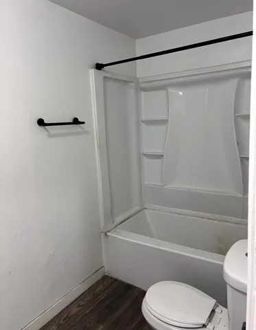 Bathroom featuring a white tub-shower combination unit, matte black shower rod, matte black towel bar, and wood-finish flooring