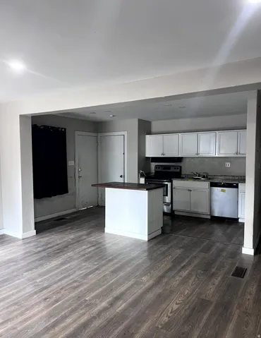 Open-concept living area featuring wood-finish flooring, recessed lighting, and a white kitchen island with a dark countertop