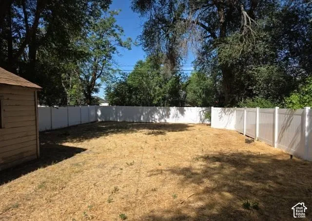 Expansive yard featuring a white privacy fence, mature trees, and a detached shed with wood siding and a shingle roof