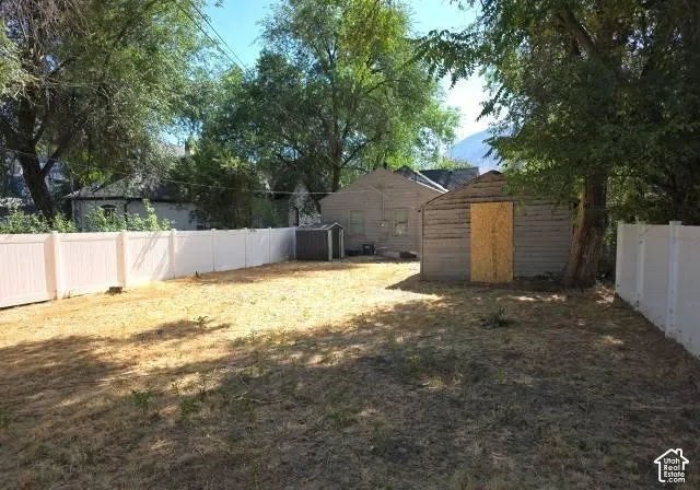 Expansive backyard featuring a white privacy fence, an accessory structure with horizontal siding, and mature trees providing shade