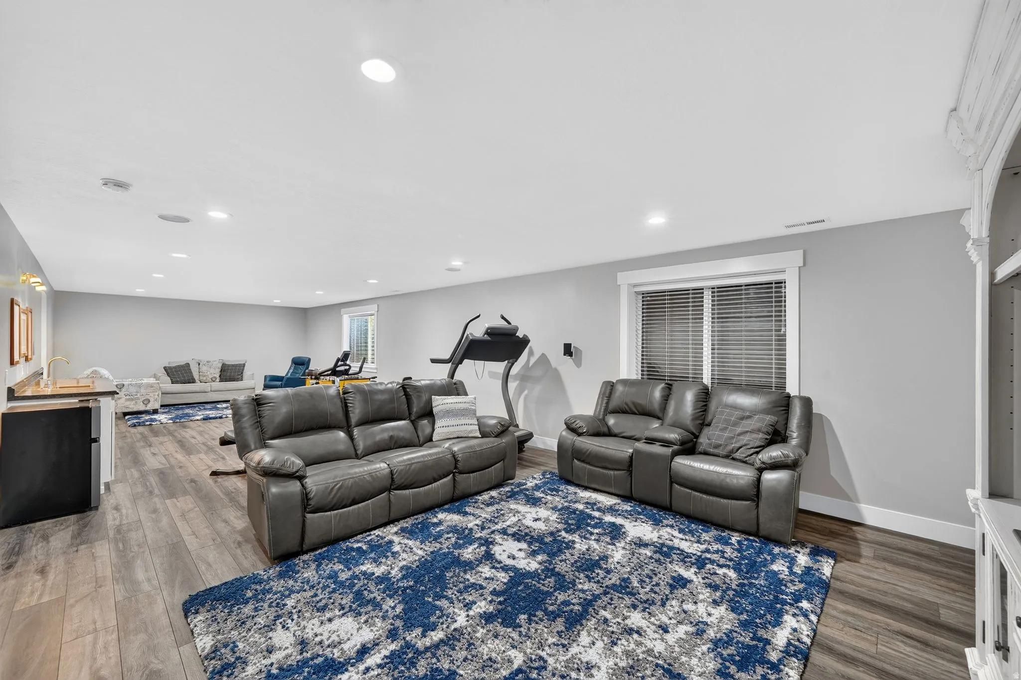 Spacious entertainment area featuring wood-finish flooring, recessed lighting, and a built-in wet bar with a compact refrigerator