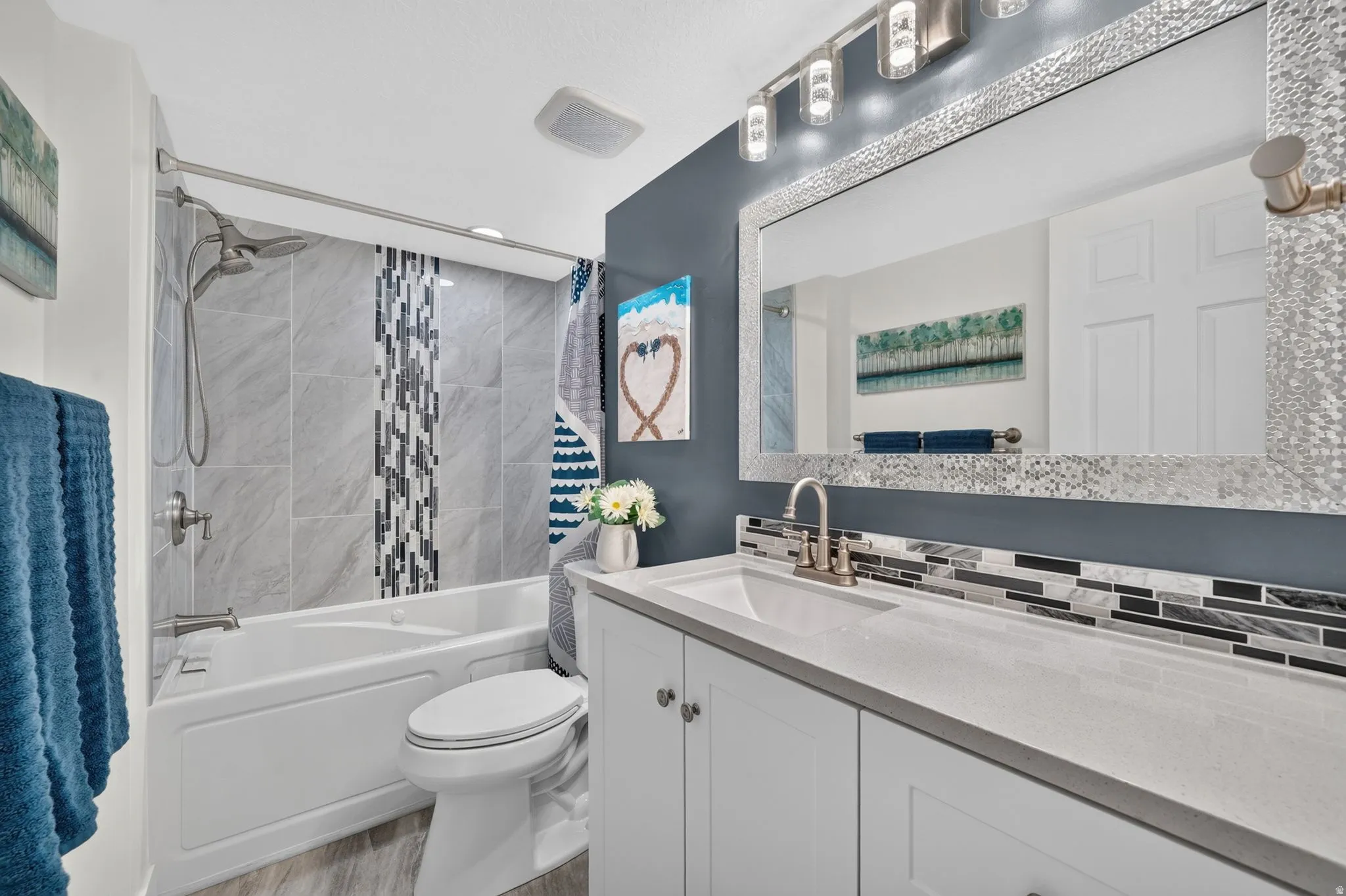 Bathroom featuring a white vanity with integrated sink, a mosaic-tiled mirror, and a full-size bathtub with a shower head and custom tile surround