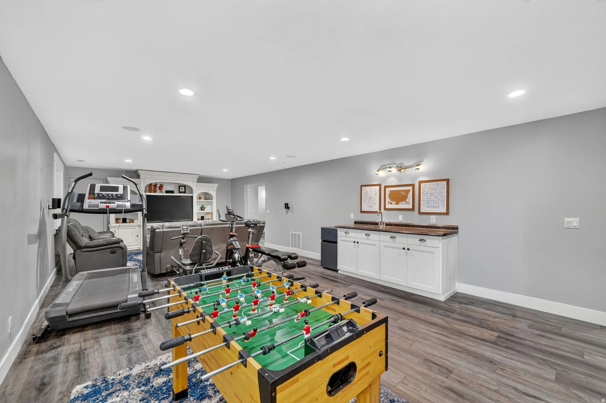 Spacious room featuring wood-finish flooring, recessed lighting, and a built-in wet bar with white cabinetry and dark countertops