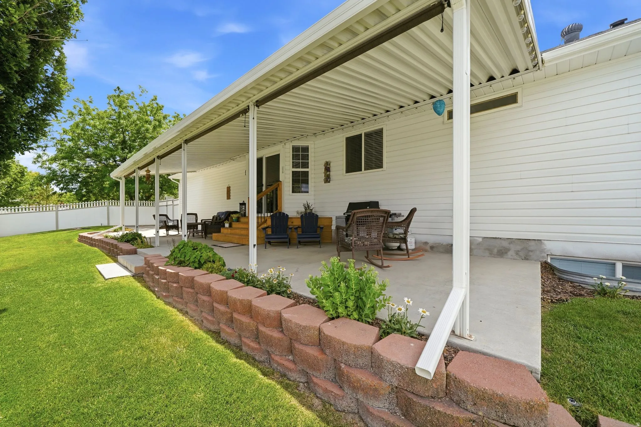 Expansive covered patio featuring a concrete surface, white vinyl siding exterior, and a white picket fence
