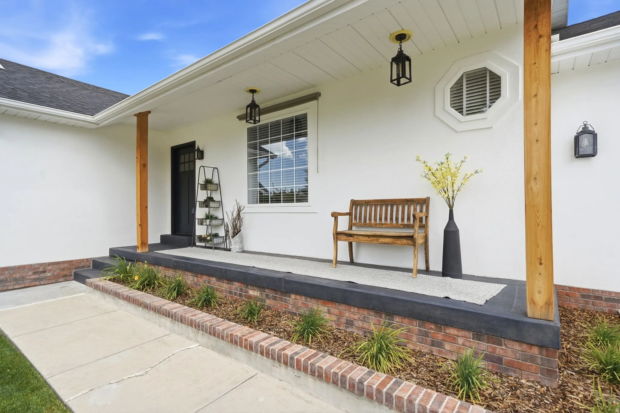 Inviting front porch featuring a dark entry door, exposed wood columns, an octagonal window, white siding, and a brick base