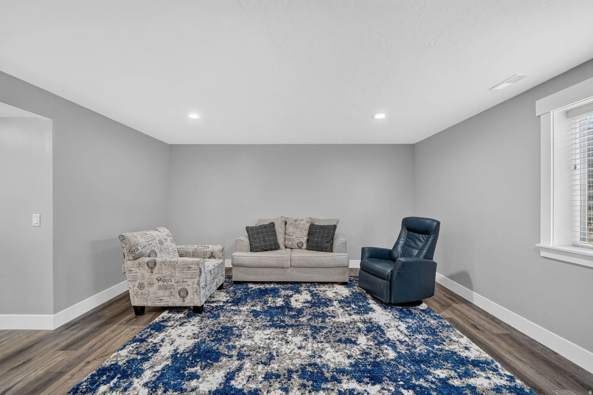Spacious room featuring wood-finish flooring, recessed lighting, a window with blinds, and white baseboards