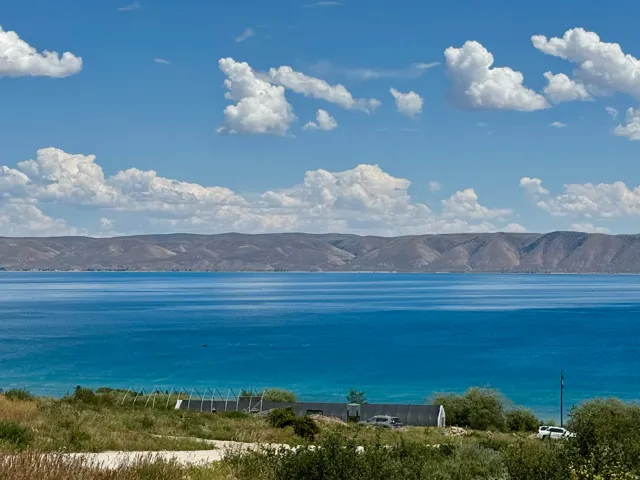 Expansive water frontage with a vibrant blue-green hue, featuring distant mountains and a natural, undeveloped shoreline