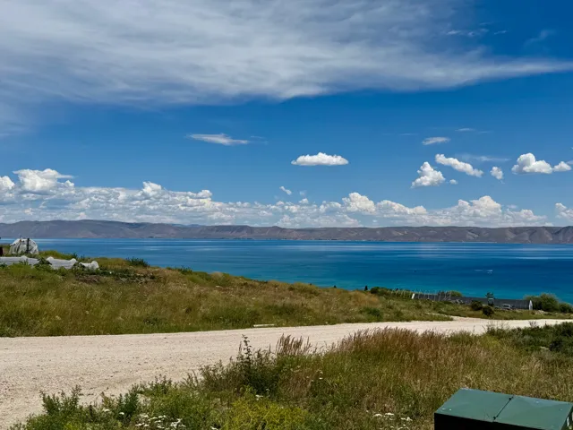 Expansive water frontage with a vibrant blue-green hue, framed by distant mountains and a clear sky