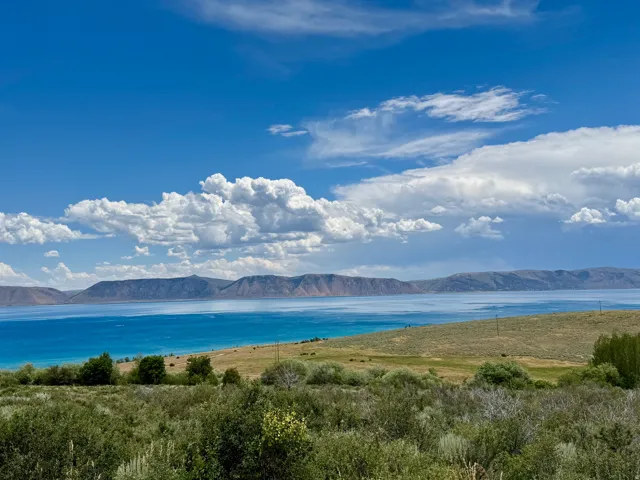 Expansive water frontage featuring a vibrant blue lake, distant mountain range, and natural shrubland