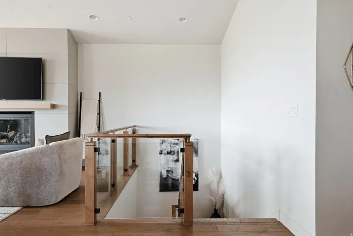 Hardwood flooring, a glass and wood-finish stair railing, and a contemporary fireplace with solid wood mantel