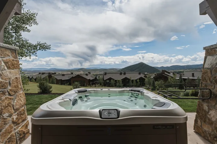 Outdoor hot tub featuring a stone-clad columns, golf course views, and mountain scenery