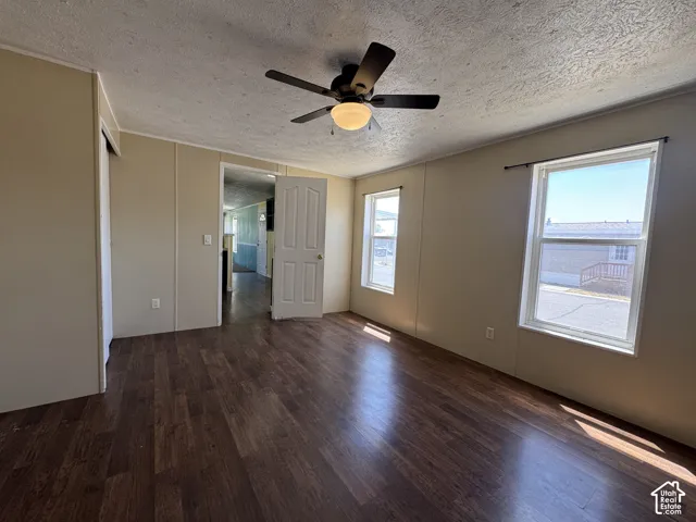 Spacious interior room featuring rich wood-finish flooring, a ceiling fan with integrated lighting, and two windows providing natural illumination