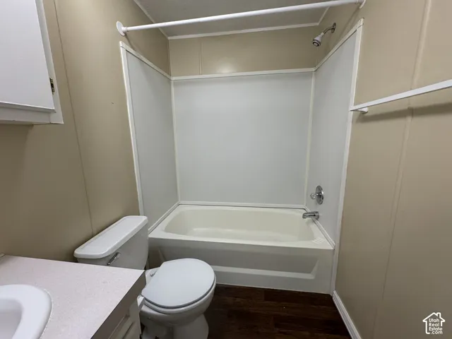 Bathroom featuring a full tub and shower combination with a white surround, chrome fixtures, dark wood-finish flooring, and a white toilet