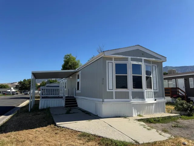 Light-gray siding exterior featuring a covered porch with white railing, a bay window with decorative shutters, and a sloped metal awning