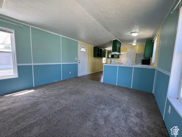 Spacious living area featuring grey carpeting, two-tone wall paneling, and an open-concept layout to the kitchen