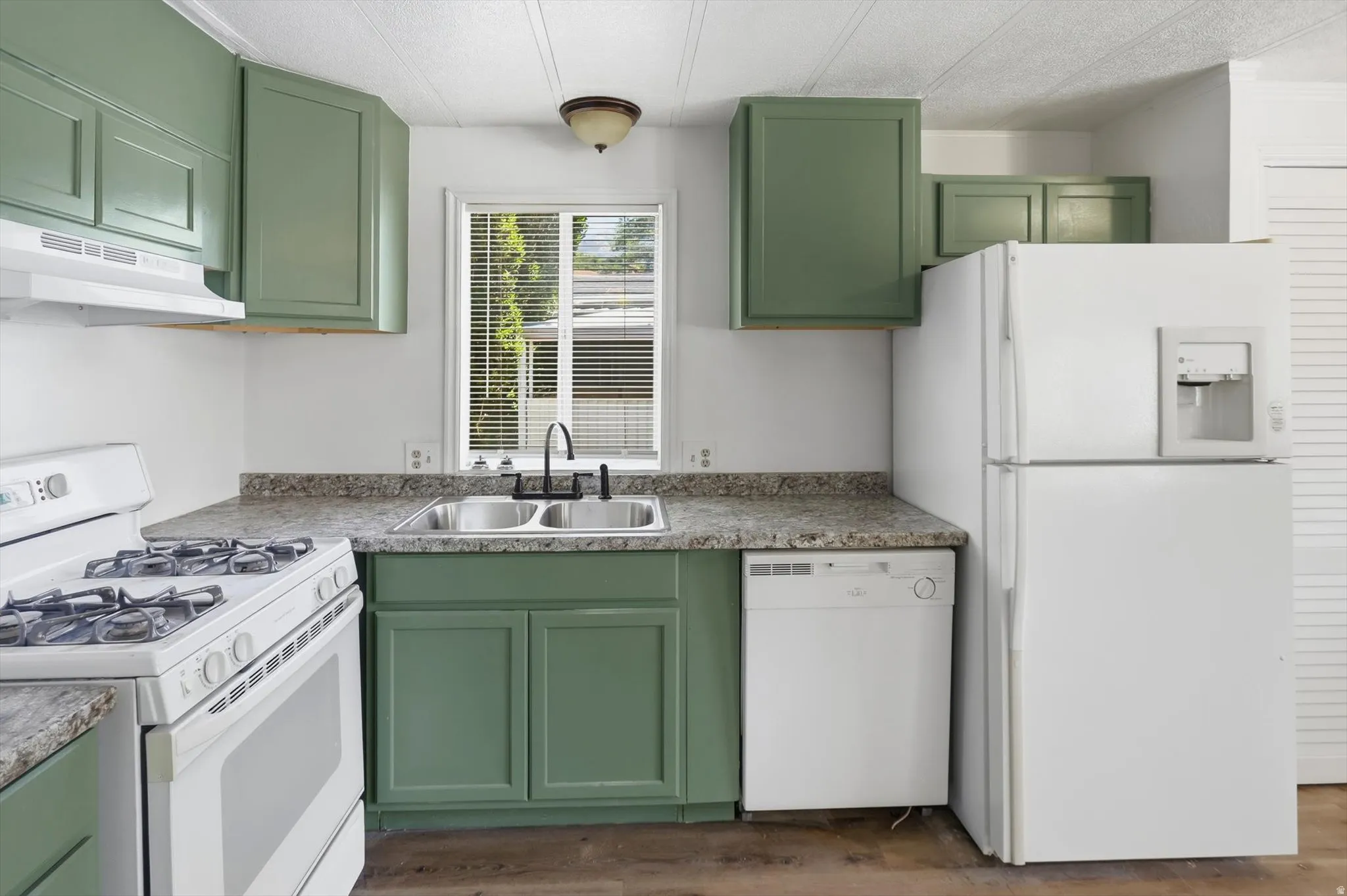 Kitchen featuring green cabinetry, a dual basin stainless steel sink with a black-finish faucet, and laminate countertops