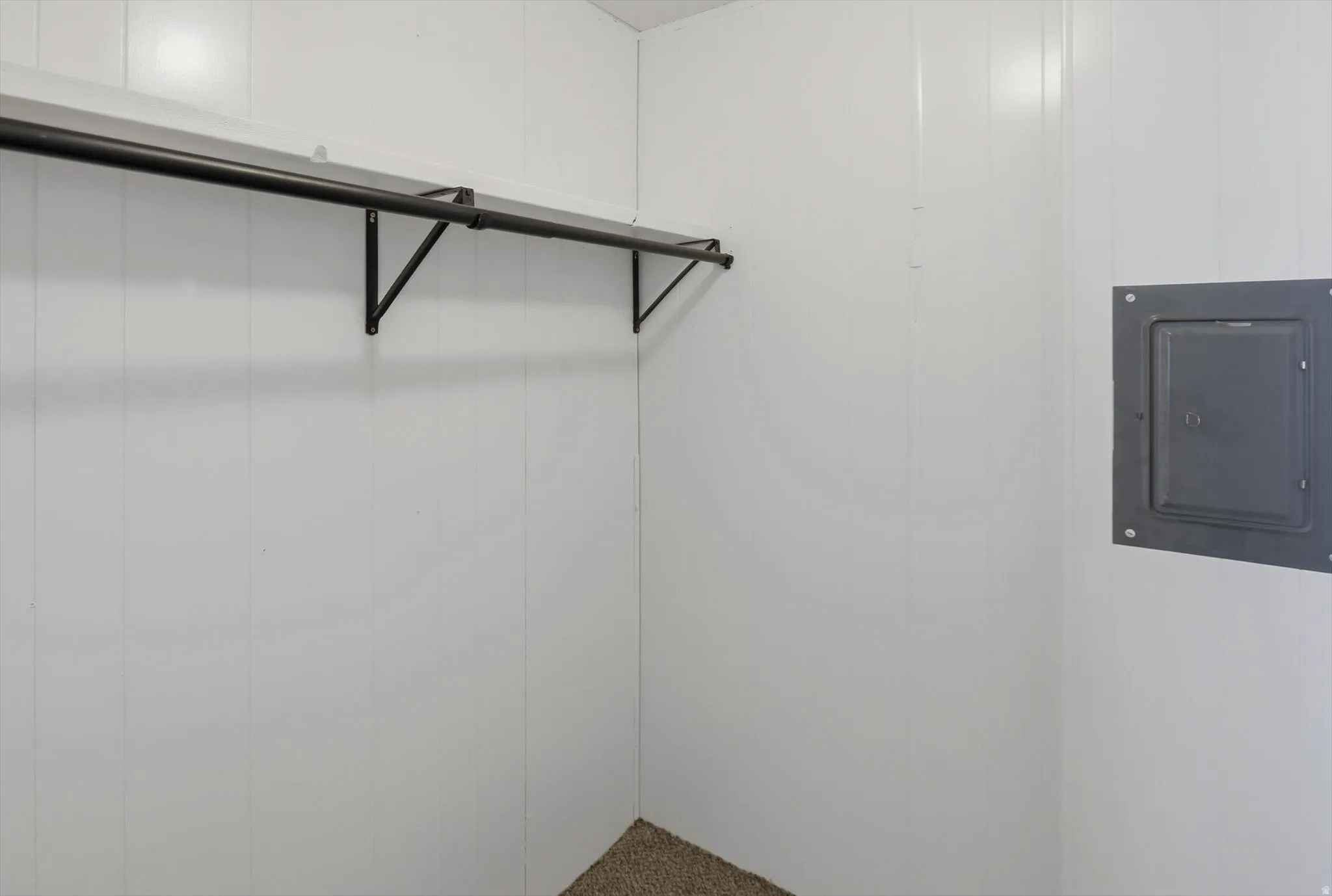 White paneled walls featuring a black metal clothing rod and a recessed utility panel