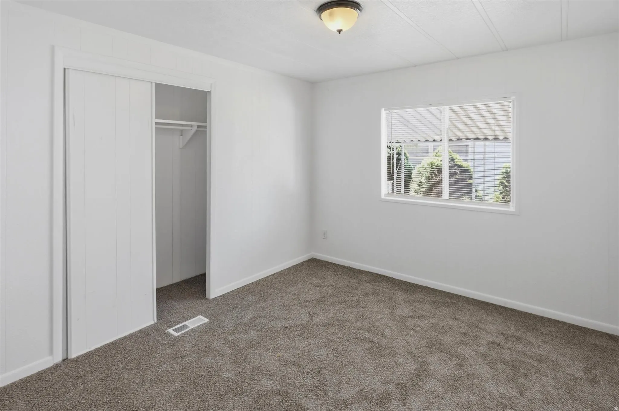 White-painted room featuring neutral-toned carpet, a window with horizontal blinds, and a built-in closet with sliding doors