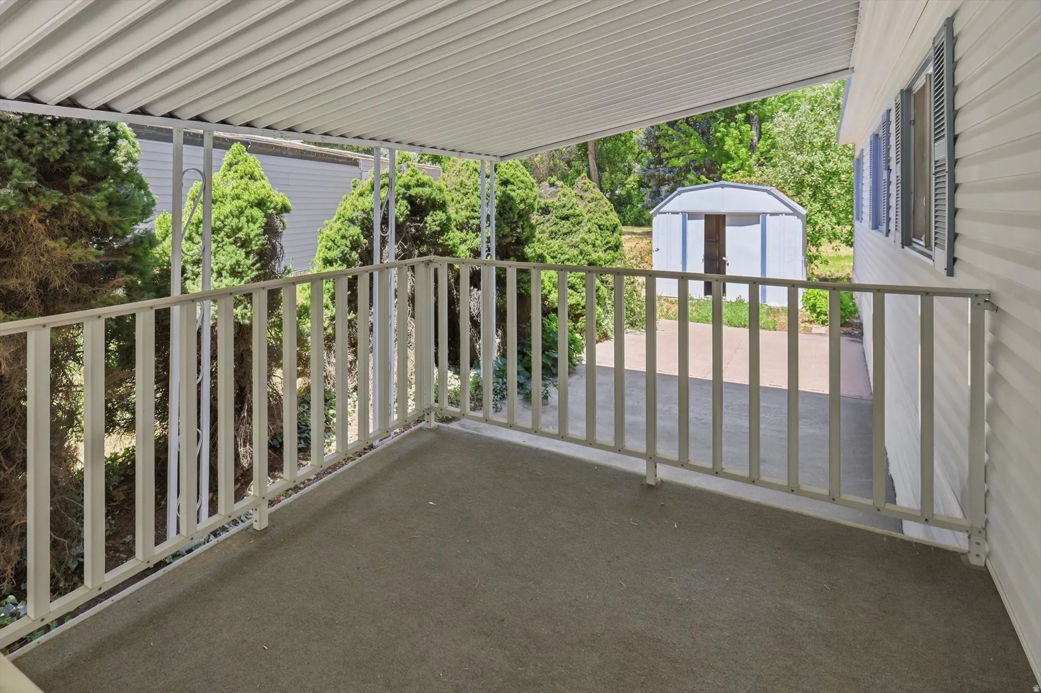 Covered patio with textured flooring, white metal railing, and a slatted overhang