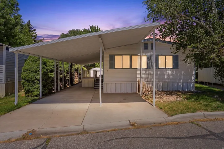 Exterior featuring white siding, a covered carport, and mature perimeter trees