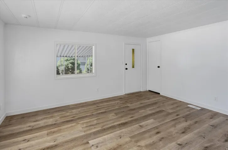 Spacious room featuring wood-finish flooring, white walls, and a window with exterior views