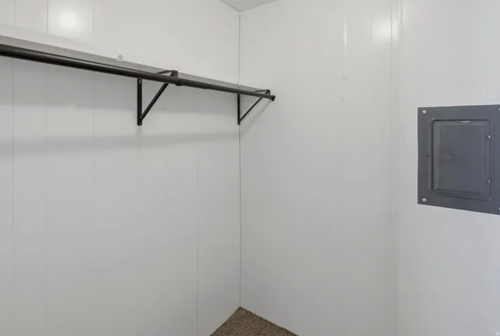 White paneled walls featuring a black metal clothing rod and a recessed utility panel