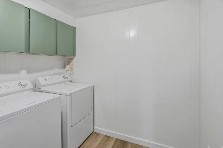Laundry area featuring green wall cabinetry, white wall paneling, and wood-finish flooring