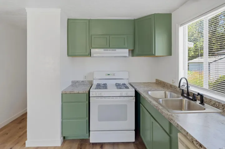 Kitchen featuring sage green cabinetry, white gas range, stainless steel double basin sink with matte black faucet, and wood-finish flooring