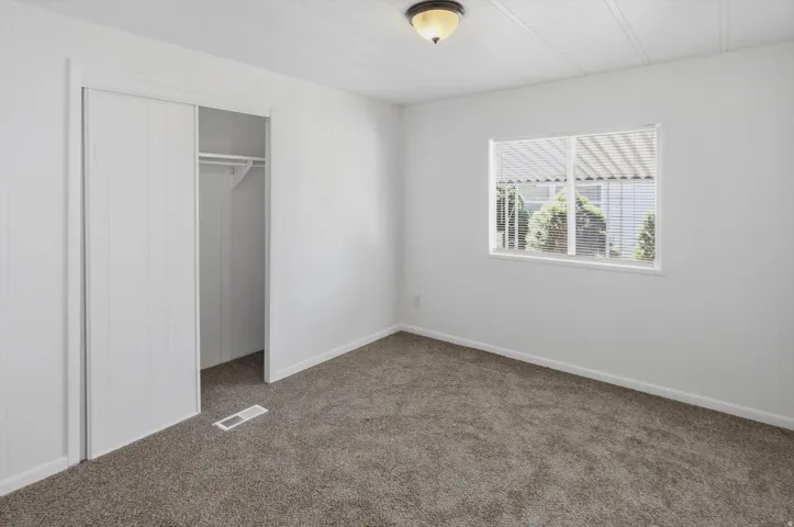 White-painted room featuring neutral-toned carpet, a window with horizontal blinds, and a built-in closet with sliding doors