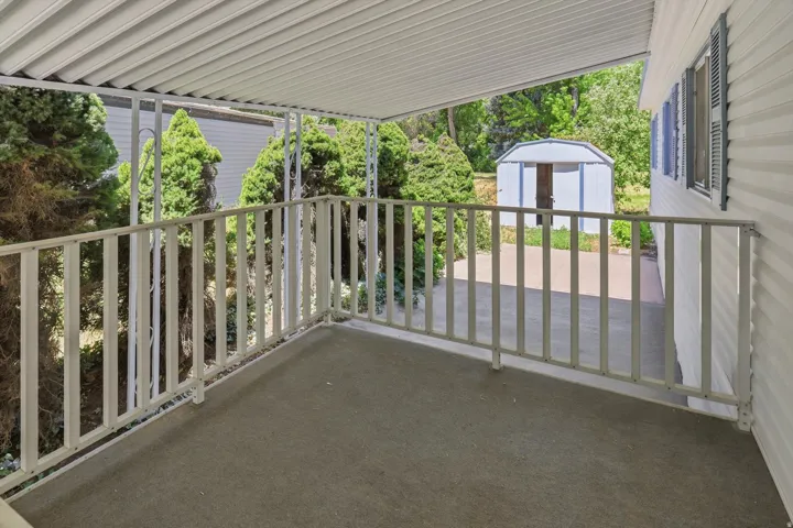Covered patio with textured flooring, white metal railing, and a slatted overhang
