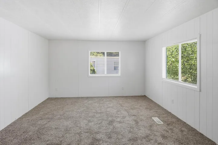 Bright interior space featuring light gray textured carpeting, white paneled walls, and two windows with white blinds