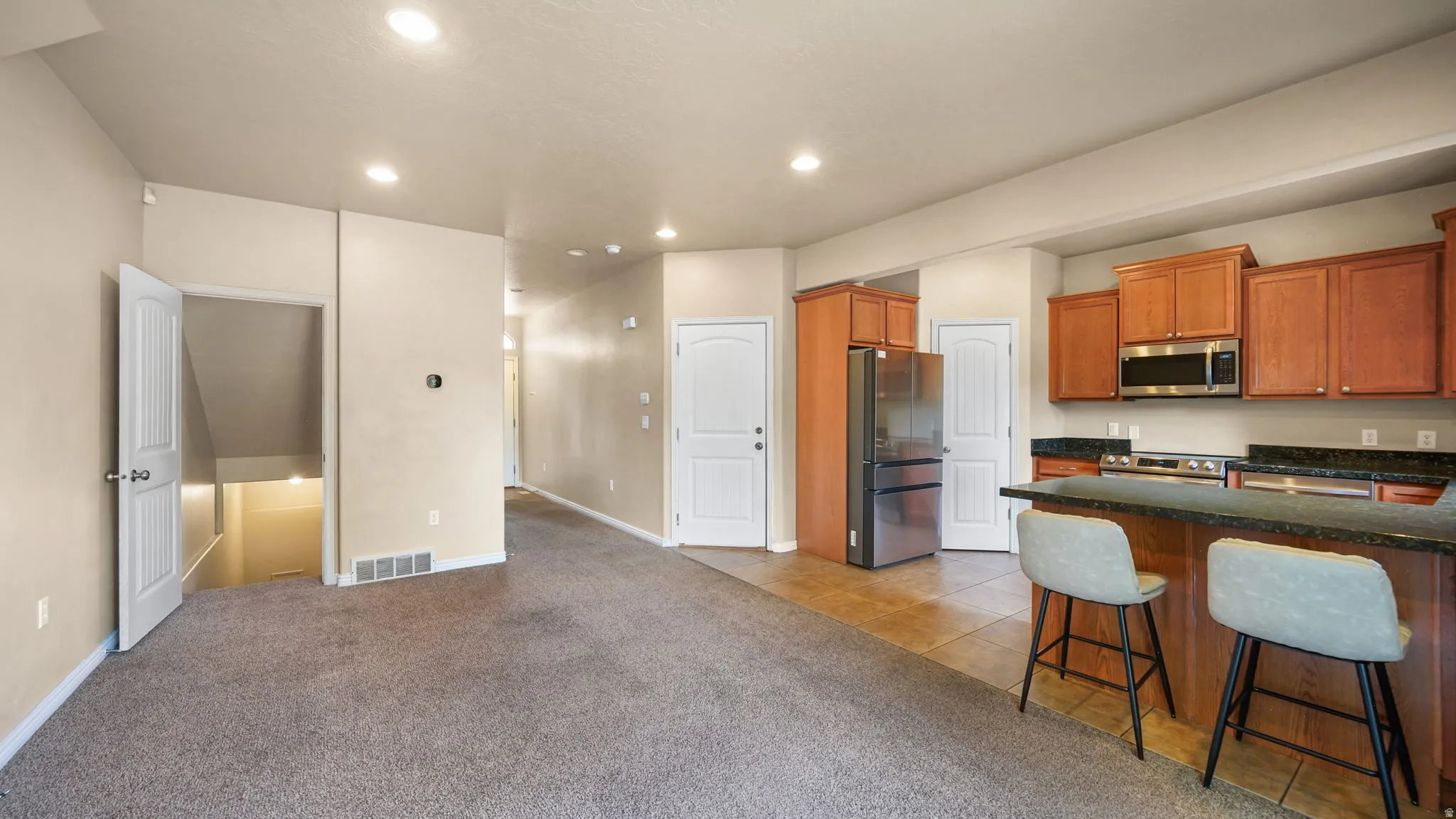 Open-concept living area featuring a kitchen with wood cabinetry, stainless steel appliances, and a breakfast bar