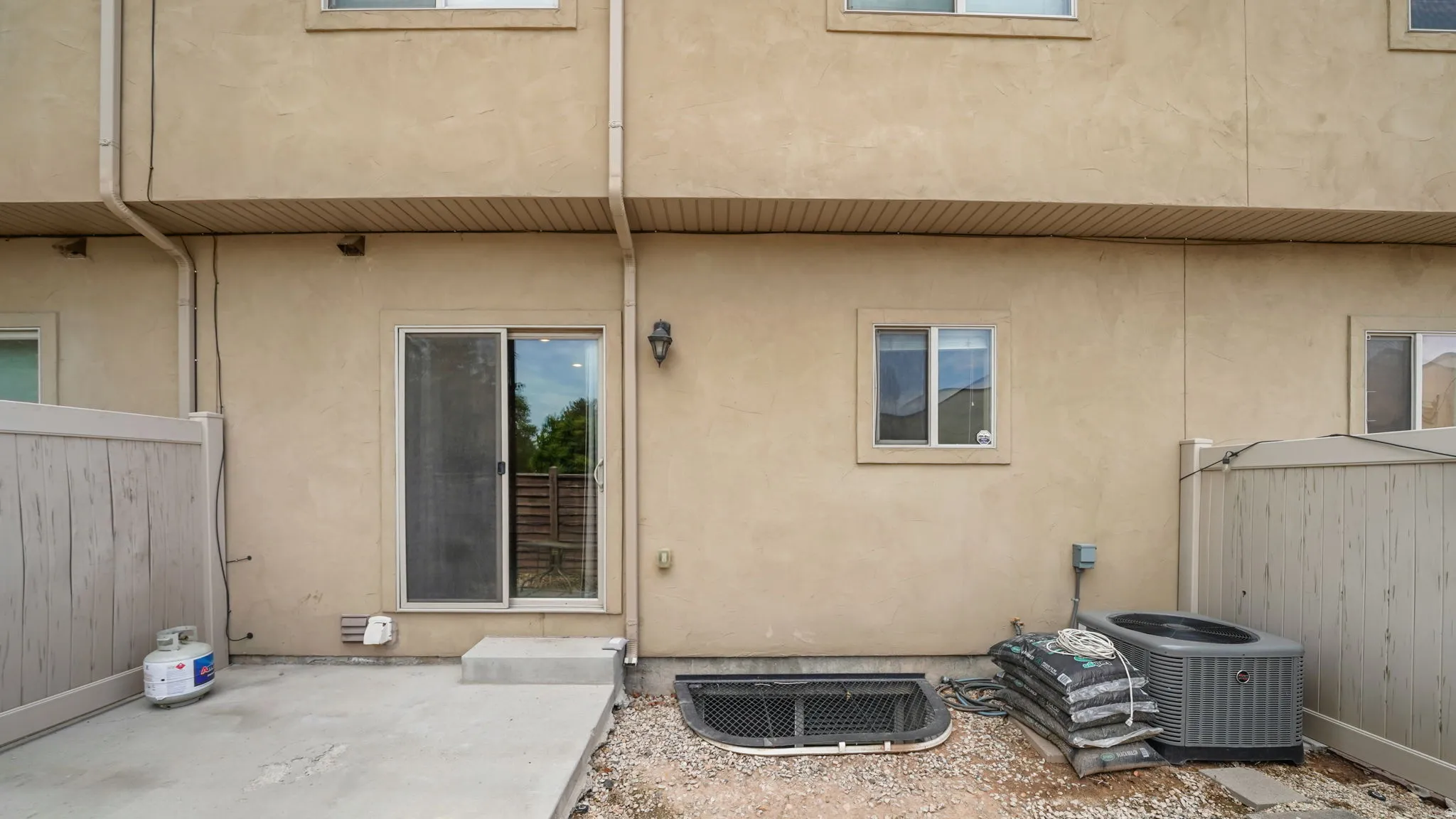 Rear patio area featuring a sliding glass door, a window well with grate, and two exterior windows