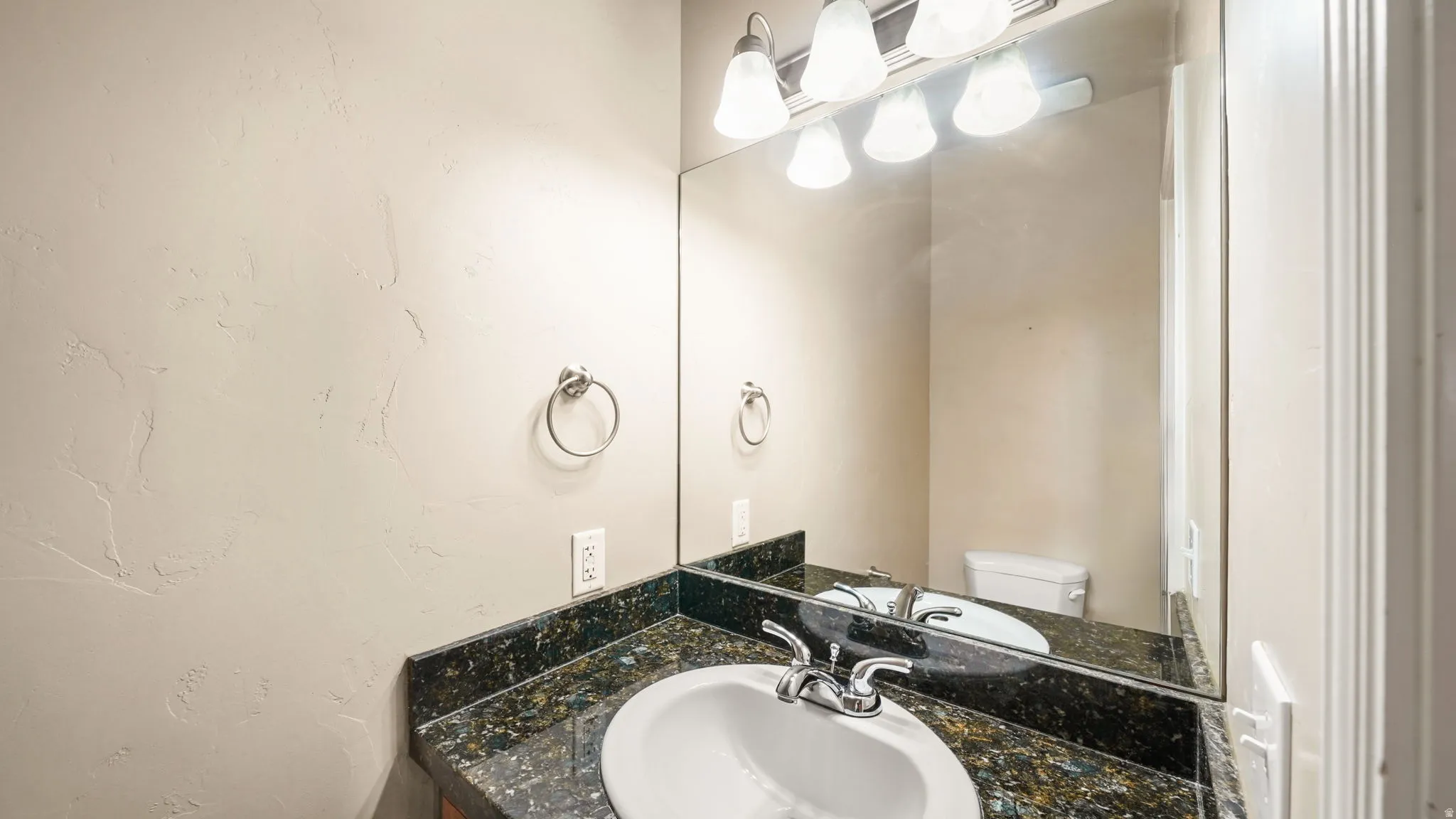 Bathroom vanity featuring a white oval sink with chrome faucet, a speckled dark countertop, and a large wall-mounted mirror
