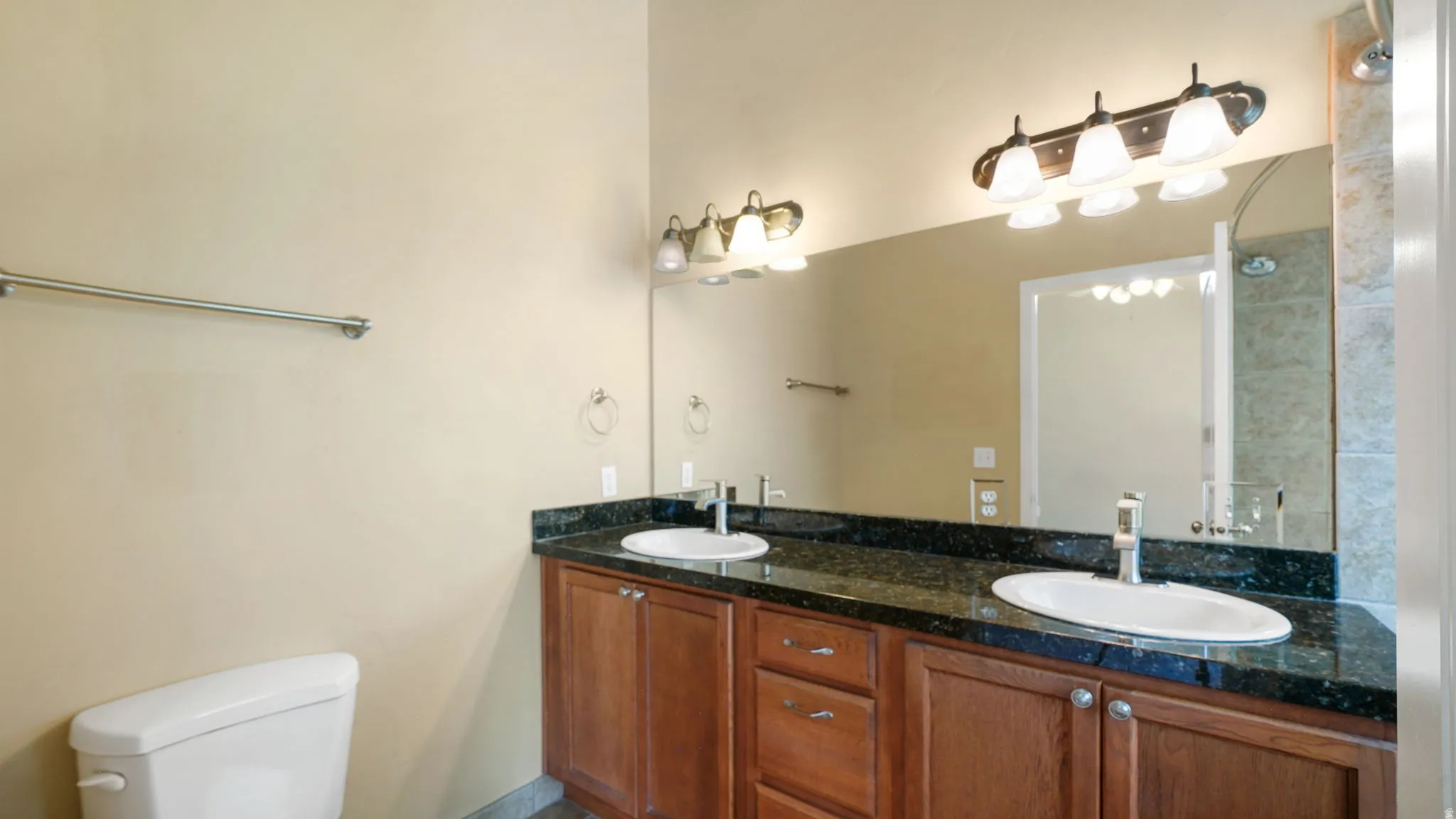 Bathroom featuring a dual vanity with a dark granite countertop, undermount sinks, and wood-finish cabinetry