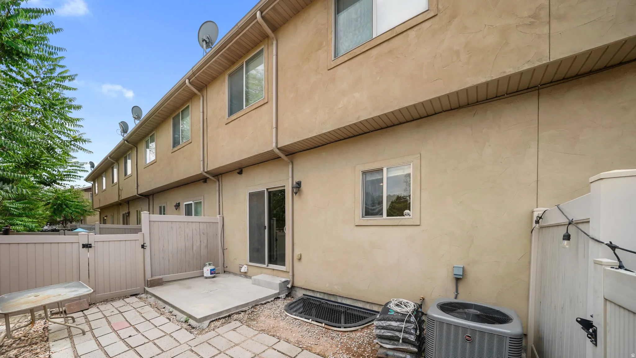 Rear exterior featuring a stucco facade, multiple windows, a sliding glass door, and an air conditioning unit