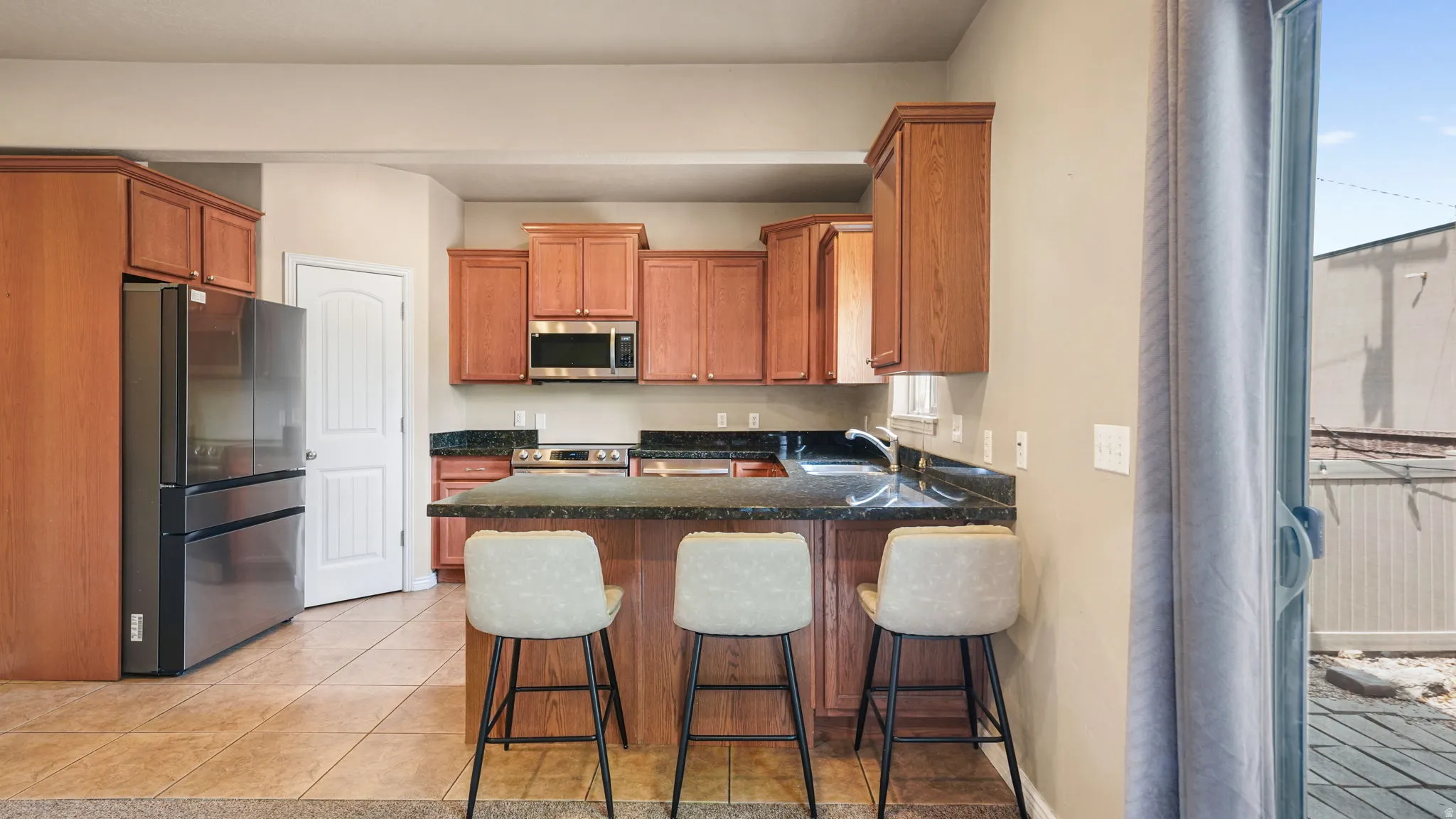 Kitchen featuring a peninsula with dark countertops, wood cabinetry, tile flooring, and stainless steel appliances