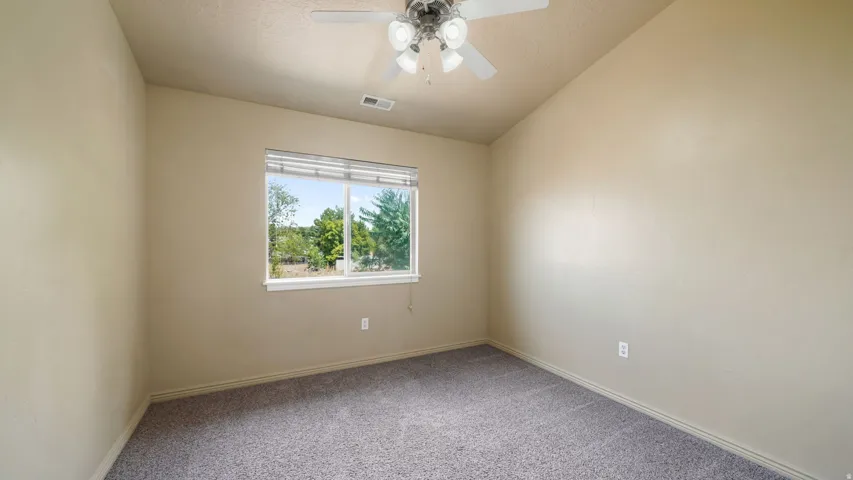 Carpeted room with a ceiling fan, a window featuring horizontal blinds, and neutral-toned walls