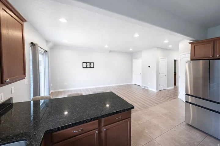 Kitchen island with dark countertop, stainless steel refrigerator, recessed lighting, wood-finish flooring, and sliding glass door