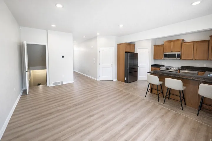 Open-concept living area with wood-finish flooring, recessed lighting, and a kitchen featuring wood cabinetry, stainless steel appliances, and a dark countertop breakfast bar