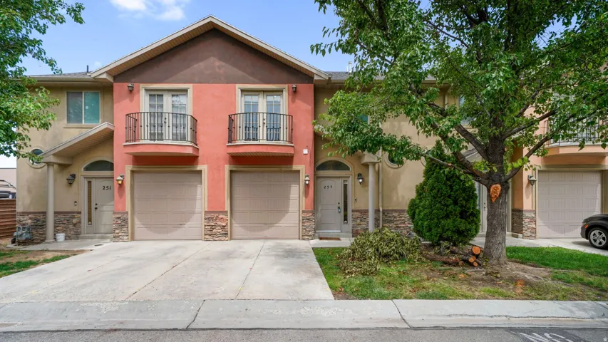 Townhome exterior featuring a two-tone stucco facade, stone accents, two attached garages, and a paved driveway