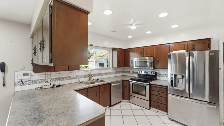 Kitchen featuring rich wood cabinetry, stainless steel appliances, a double basin sink, ample counter space, and recessed lighting