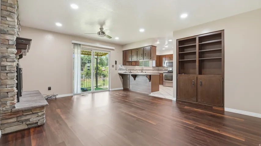 Open-concept living area featuring rich wood-finish flooring, a stacked stone fireplace, and recessed lighting