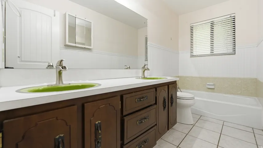 Bathroom featuring a dual-sink vanity with a white countertop and wood-finish cabinetry, a toilet, and a bathtub with a window above