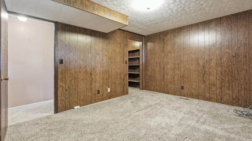 Spacious room featuring wood-finish paneling, textured ceiling, and neutral-toned carpeting