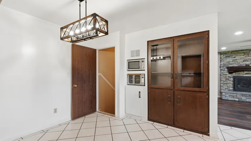 Tiled flooring extending into an area featuring a wood-finish cabinet with glass panel doors, integrated microwave, and an additional appliance bay