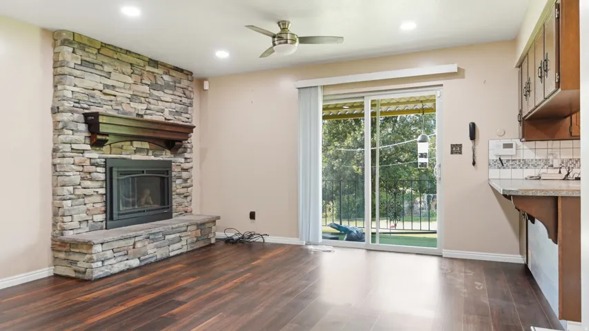 Stacked stone fireplace with a dark wood mantel and hearth, wood-finish flooring, recessed lighting, and a ceiling fan