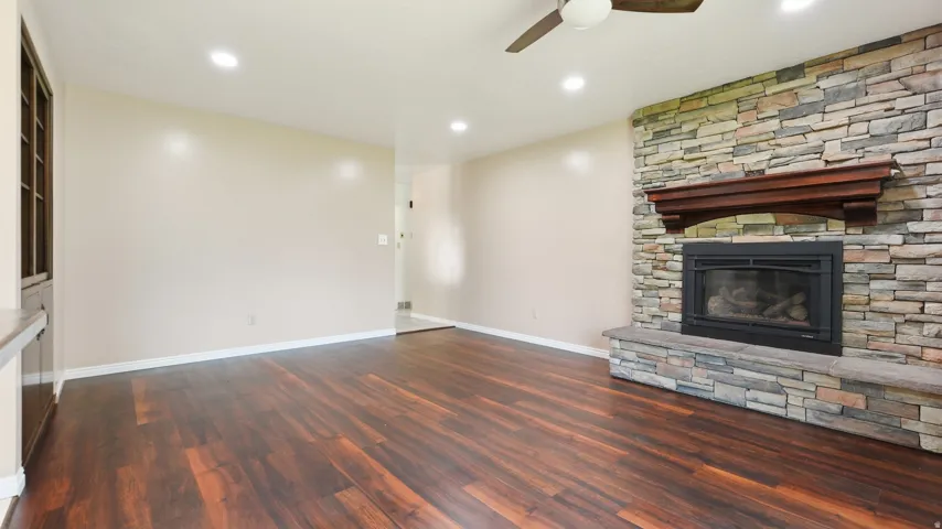 Spacious room featuring a stacked stone fireplace with a substantial wood mantle, wood-finish flooring, recessed lighting, and a ceiling fan